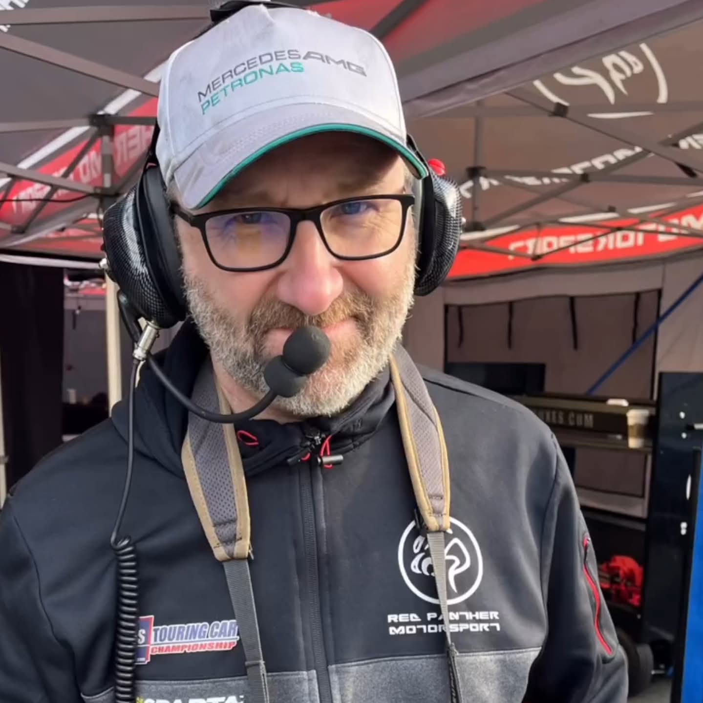 Tim McGraw wearing a radio headset and Red Panther Motorsport team jacket at the track